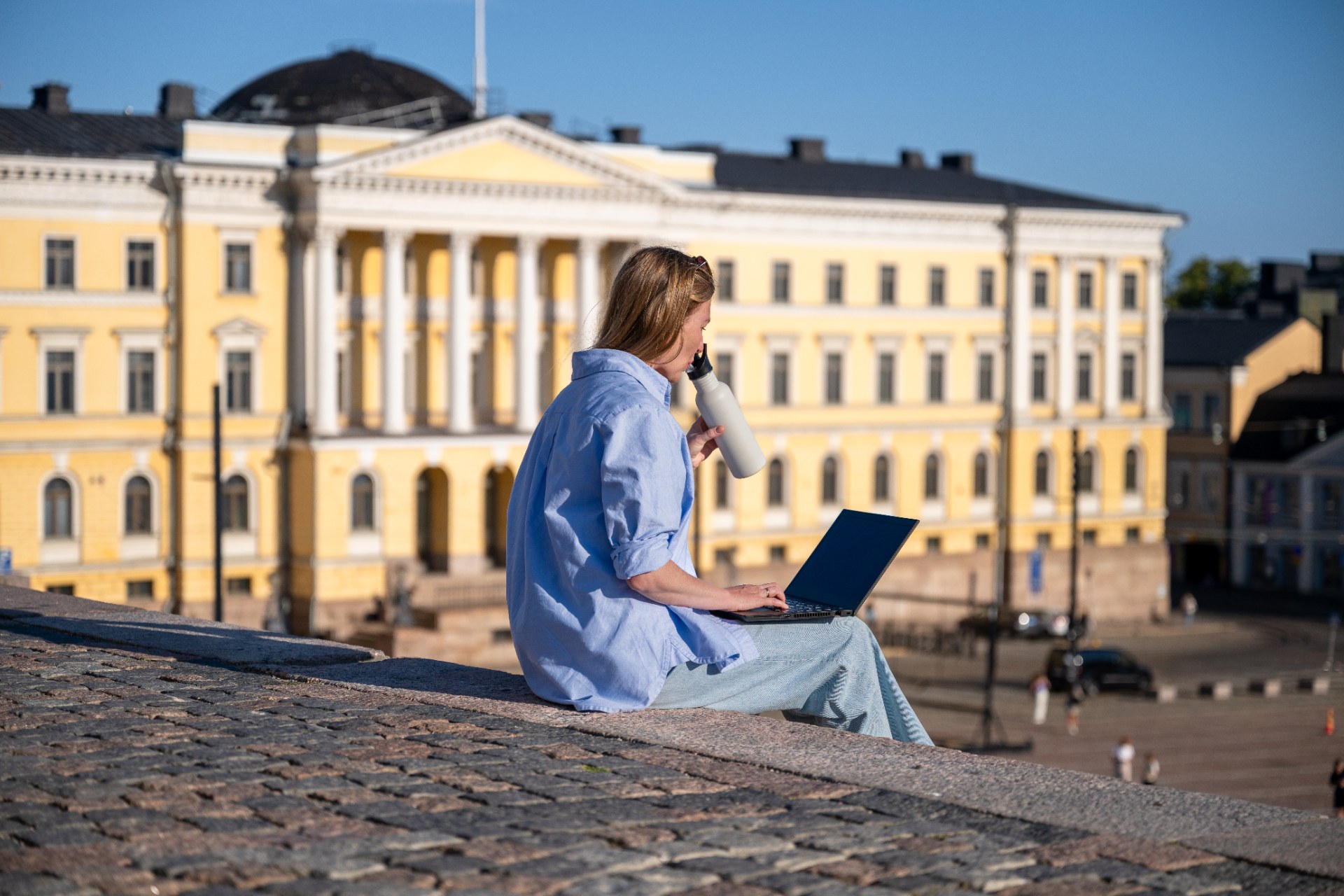 Mujer joven con una laptop sentada en las escalinatas de la plaza del Senado de Helsinki